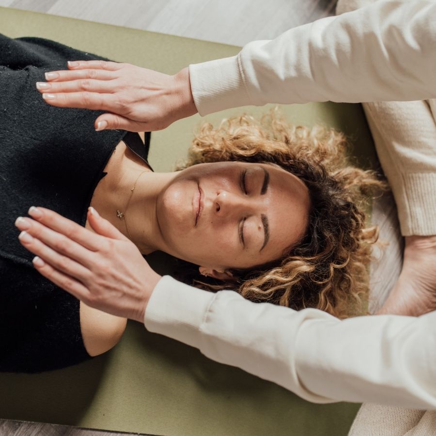 Frau liegt entspannt auf einer Liege während einer Reiki Sitzung mit achtsam aufgelegten Händen zur Förderung von innerer Ruhe und Balance